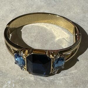 Emerald-cut deep blue gemstone, which is flanked by two oval-shaped blue stones